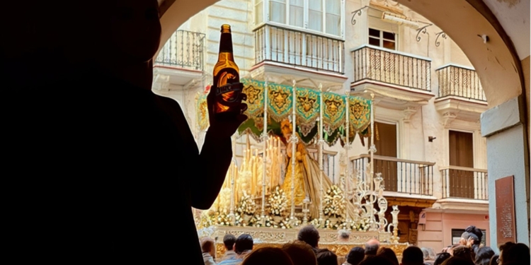 Persona con una cerveza en la mano en el Arco del Pópulo mientras pasa la Vírgen de las Penas en semana santa