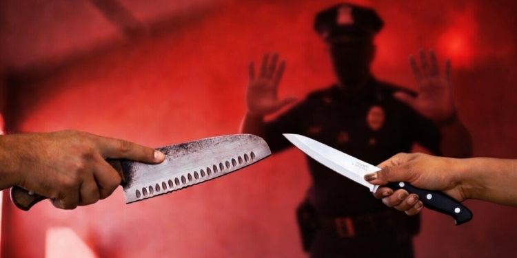 Dos personas enfrentándose con cuchillos mientras un policía intenta intervenir al fondo en una escena de tensión y violencia.