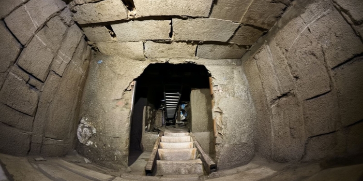 Entrada a una cámara subterránea de piedra con escaleras estrechas, similar a un túnel antiguo o pasadizo oculto.