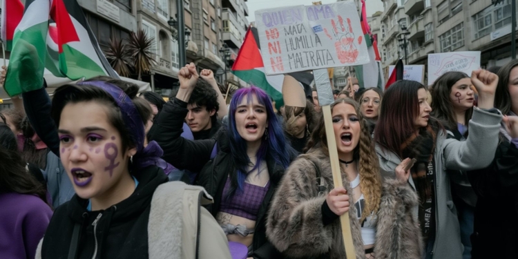 Manifestación feminista en una ciudad con jóvenes protestando, pancartas reivindicativas y símbolos de igualdad en el rostro