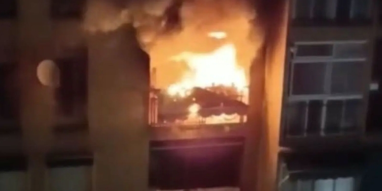 Incendio en el interior de un edificio visto desde una ventana, con llamas intensas y humo en un entorno urbano.