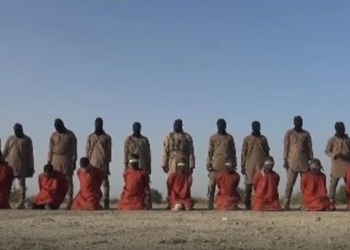Grupo de hombres vestidos de naranja arrodillados frente a individuos armados en un entorno desértico, escena asociada a propaganda terrorista.