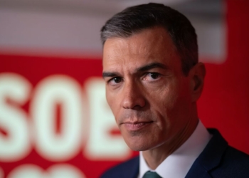 Pedro Sánchez en primer plano con fondo rojo del PSOE durante un acto político.