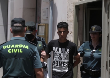 Agentes de la Guardia Civil trasladando a un joven detenido a la salida de un edificio en un entorno urbano.