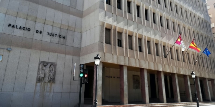 Fachada de un edificio institucional con el rótulo “Palacio de Justicia”, con varias banderas oficiales en la entrada y un semáforo peatonal en primer plano.