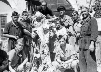 Fotografía en blanco y negro de un grupo de hombres armados posando junto a lo que parece un cuerpo o restos humanos, en un entorno rural o de conflicto.