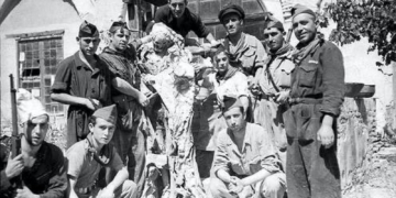 Fotografía en blanco y negro de un grupo de hombres armados posando junto a lo que parece un cuerpo o restos humanos, en un entorno rural o de conflicto.