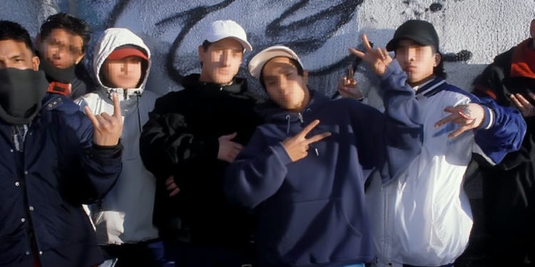 Grupo de jóvenes con el rostro pixelado posando juntos frente a un muro con grafitis, haciendo gestos con las manos y vistiendo ropa urbana.