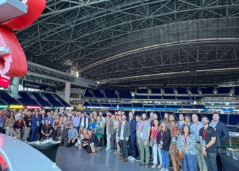 Grupo numeroso de personas posando en el interior de un gran estadio cubierto, con gradas azules al fondo y una estructura metálica en el techo, durante un evento de Startup Olé