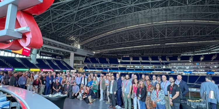 Grupo numeroso de personas posando en el interior de un gran estadio cubierto, con gradas azules al fondo y una estructura metálica en el techo, durante un evento de Startup Olé