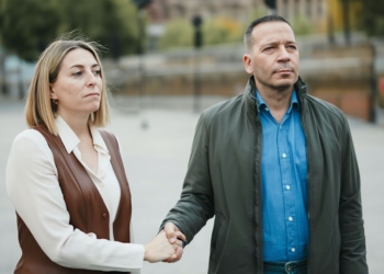 María Guardiola y Óscar Fernández de pie en la calle, dándose la mano con gesto serio mientras miran hacia el frente.
