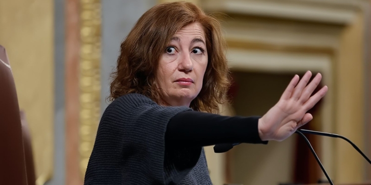 Francina Armengol en el Congreso de los Diputados levanta la mano en gesto de detener o pedir silencio, con expresión seria mientras habla frente a un micrófono.