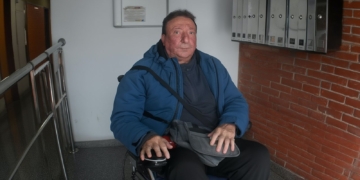 Pepe en silla de ruedas dentro de un portal, junto a buzones de correo, mira al frente con expresión seria.