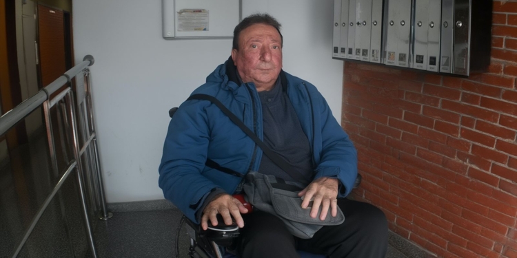 Pepe en silla de ruedas dentro de un portal, junto a buzones de correo, mira al frente con expresión seria.