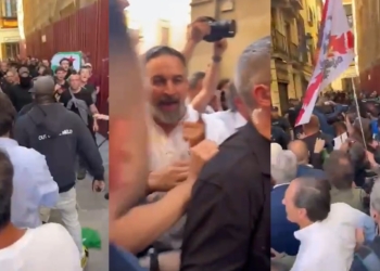 Santiago Abascal entre la multitud en una calle estrecha durante un intento de frenar que interrumpieran un mitin de Vox en Granada por parte de Antifascistas, con empujones y tensión, personas grabando con móviles y una bandera visible entre la gente.