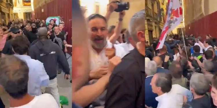 Santiago Abascal entre la multitud en una calle estrecha durante un intento de frenar que interrumpieran un mitin de Vox en Granada por parte de Antifascistas, con empujones y tensión, personas grabando con móviles y una bandera visible entre la gente.