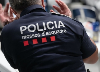 Espalda de un agente de policía con uniforme que muestra el texto “Policia mossos d’esquadra”, en un entorno interior.