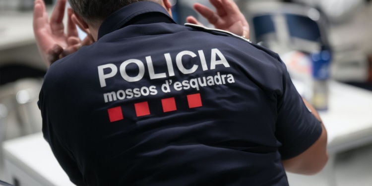Espalda de un agente de policía con uniforme que muestra el texto “Policia mossos d’esquadra”, en un entorno interior.