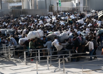 Gran multitud de personas concentradas en un paso fronterizo o acceso controlado, muchas cargando bolsas y pertenencias voluminosas, avanzando de forma aglomerada entre vallas metálicas.