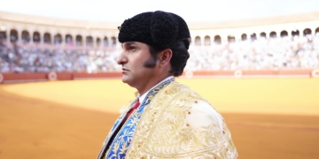 El Torero Jose Antonio Morante de la Puebla vestido con traje de luces y montera, de perfil en una plaza de toros llena de público al fondo.