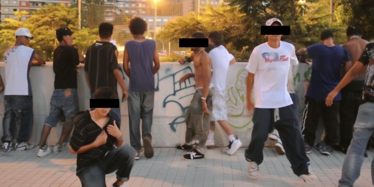 Grupo de jóvenes en un entorno urbano, algunos apoyados en un muro con grafitis; varios rostros están cubiertos con franjas negras para ocultar la identidad.