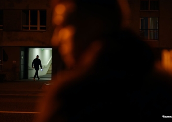 Persona entrando en un edificio iluminado por la noche, con una figura desenfocada en primer plano.