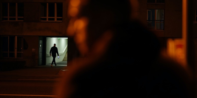 Persona entrando en un edificio iluminado por la noche, con una figura desenfocada en primer plano.
