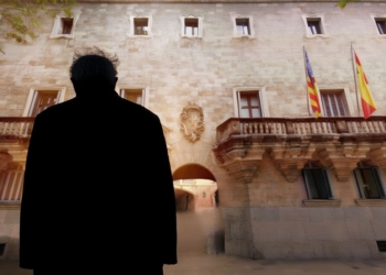 Silueta de una persona mayor frente a un edificio institucional con banderas de España, la Unión Europea y una bandera regional.