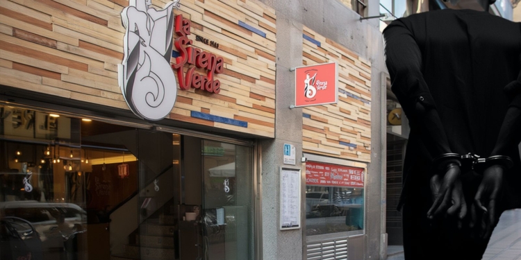 Fachada de un restaurante en una calle urbana con una figura humana esposada en primer plano.