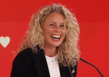 Portavoz del PSOE Montse Mínguez sonríe durante una intervención pública frente a un fondo rojo con micrófonos.