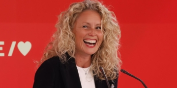 Portavoz del PSOE Montse Mínguez sonríe durante una intervención pública frente a un fondo rojo con micrófonos.