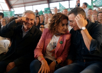 Zapatero, Maria Jesús Montero y Pedro Sánchez conversan durante un acto político rodeados de asistentes y banderas