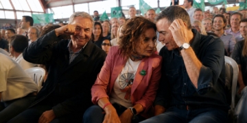 Zapatero, Maria Jesús Montero y Pedro Sánchez conversan durante un acto político rodeados de asistentes y banderas