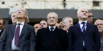 Florentino Pérez en el Bernabéu con varios directivos y asistentes vestidos de traje observan un evento desde la grada.