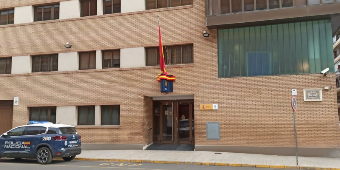 Referencia a la Brutal agresión a embarazada en Alcira Edificio de la Policía Nacional en Alcira con un coche patrulla estacionado en la entrada y una bandera de España colocada a media asta.