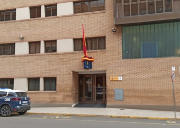 Referencia a la Brutal agresión a embarazada en Alcira Edificio de la Policía Nacional en Alcira con un coche patrulla estacionado en la entrada y una bandera de España colocada a media asta.
