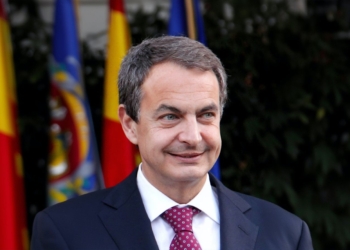 Zapatero imputado por blanqueo de capitales. José Luis Rodríguez Zapatero sonríe durante un acto oficial con banderas de España y la Unión Europea al fondo.