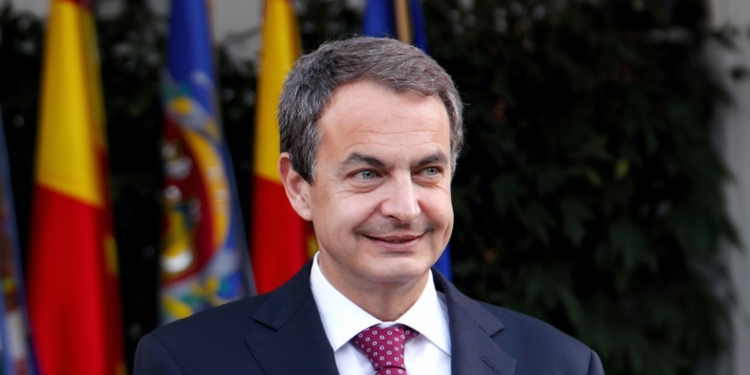 Zapatero imputado por blanqueo de capitales. José Luis Rodríguez Zapatero sonríe durante un acto oficial con banderas de España y la Unión Europea al fondo.