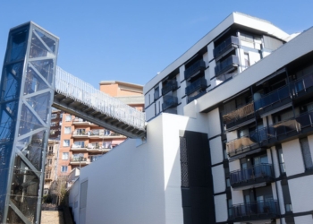 Lugar donde Un magrebí reincidente fracturó la clavícula a una anciana e intentó ahogar a su marido en Bilbao. Edificio residencial moderno con una pasarela elevada conectada a una torre metálica exterior.