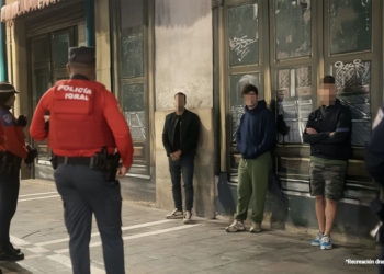 4 inmigrantes ilegales apuñalan a un hombre por sus zapatillas. Agentes de la Policía Foral vigilan a varios jóvenes apoyados contra la pared en una calle urbana.