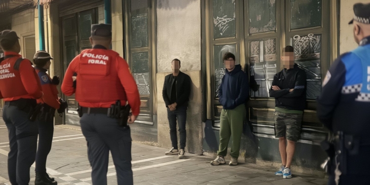 4 inmigrantes ilegales apuñalan a un hombre por sus zapatillas. Agentes de la Policía Foral vigilan a varios jóvenes apoyados contra la pared en una calle urbana.