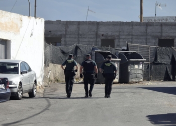 El Ejido: magrebí mata a 2 personas, deja 2 adultos y 2 bebés heridos: tres agentes de la Guardia Civil caminan por una calle industrial junto a contenedores y vehículos estacionados.