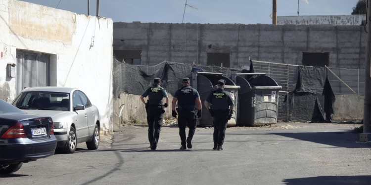 El Ejido: magrebí mata a 2 personas, deja 2 adultos y 2 bebés heridos: tres agentes de la Guardia Civil caminan por una calle industrial junto a contenedores y vehículos estacionados.