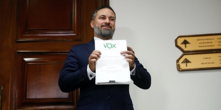 Abascal pide moción de censura tras la imputación a Zapatero. sostiene un documento con el logotipo de VOX en el interior de un edificio oficial.