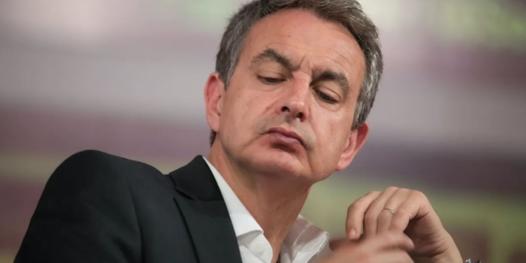 ¿Fuga a Caracas? Zapatero y su sospechoso plan de vuelo: Primer plano de Zapatero con traje oscuro y expresión seria durante un acto público.