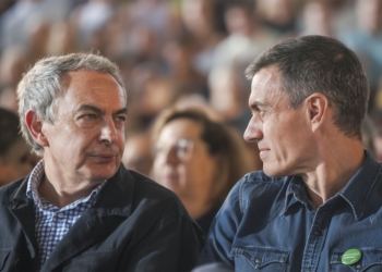 Trama Zapatero y Plus Ultra. Dos hombres conversan sentados entre el público durante un acto.