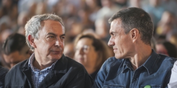 Trama Zapatero y Plus Ultra. Dos hombres conversan sentados entre el público durante un acto.