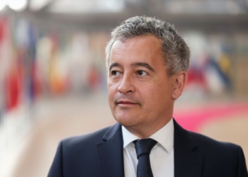 Francia dice "basta" y suspende la inmigración legal. Gerald Darmanin on traje oscuro en un espacio institucional con banderas al fondo.