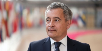 Francia dice "basta" y suspende la inmigración legal. Gerald Darmanin on traje oscuro en un espacio institucional con banderas al fondo.