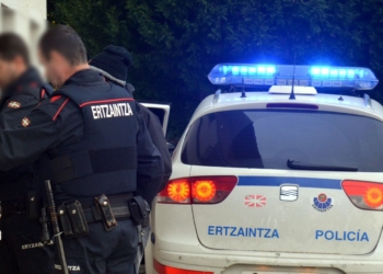 Un senegalés y un latinoamerciano agreden a sus respectivos compañeros de piso. Agentes de la Ertzaintza junto a un vehículo policial con luces azules encendidas.